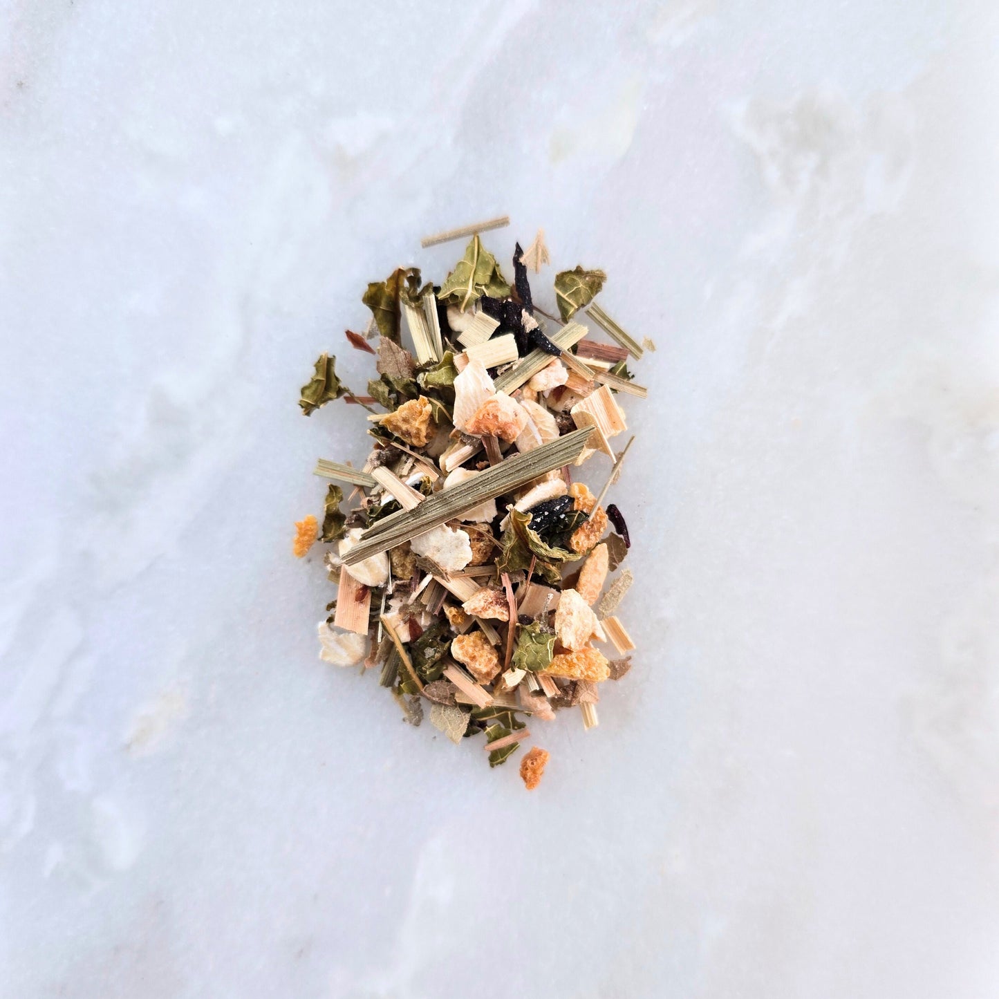 Heap of dried herbs and leaves on a light marble surface