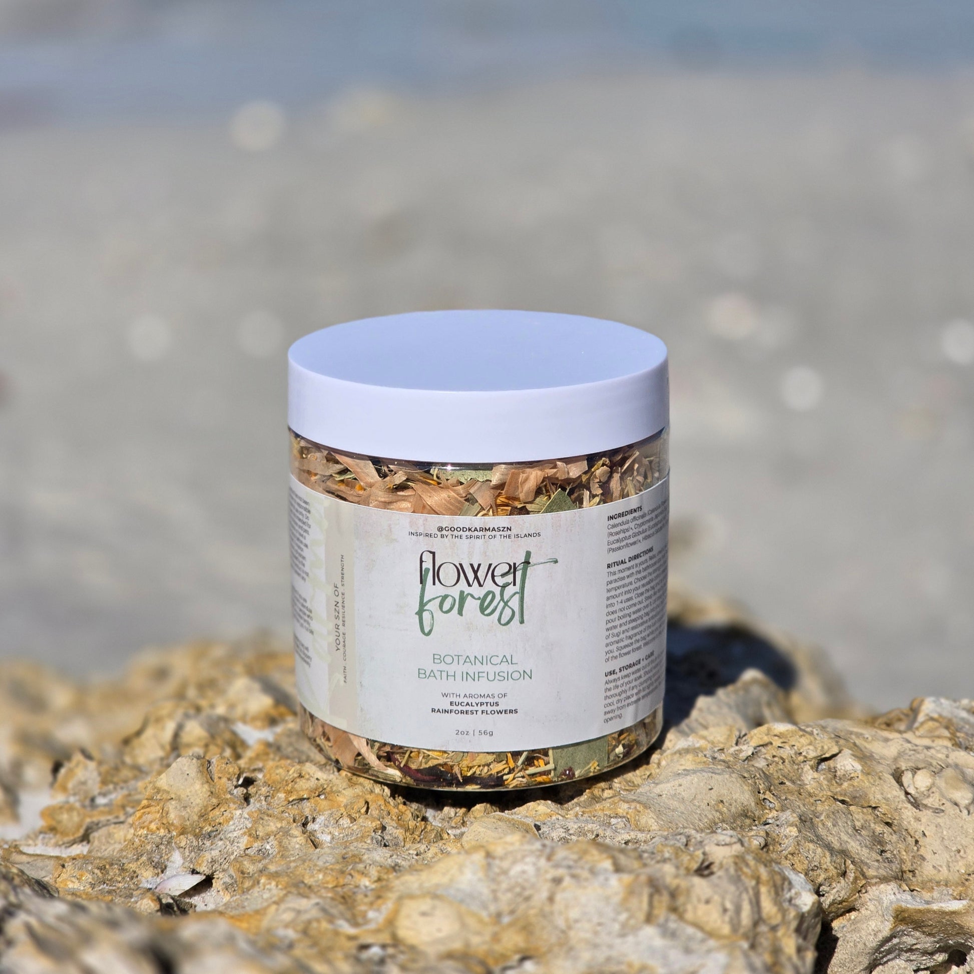 Jar of 'Flower Forest' botanical bath infusion on a rocky surface with a beach background