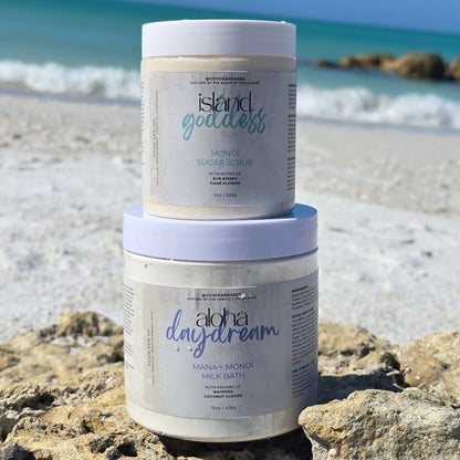 Two containers of Island Goddess and Aloha Daydream products on a beach.