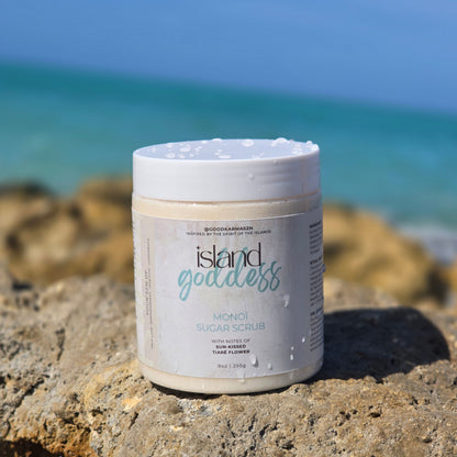 Container of whipped sugar scrub name Island Goddess on ocean rocks with the ocean and sky behind it.