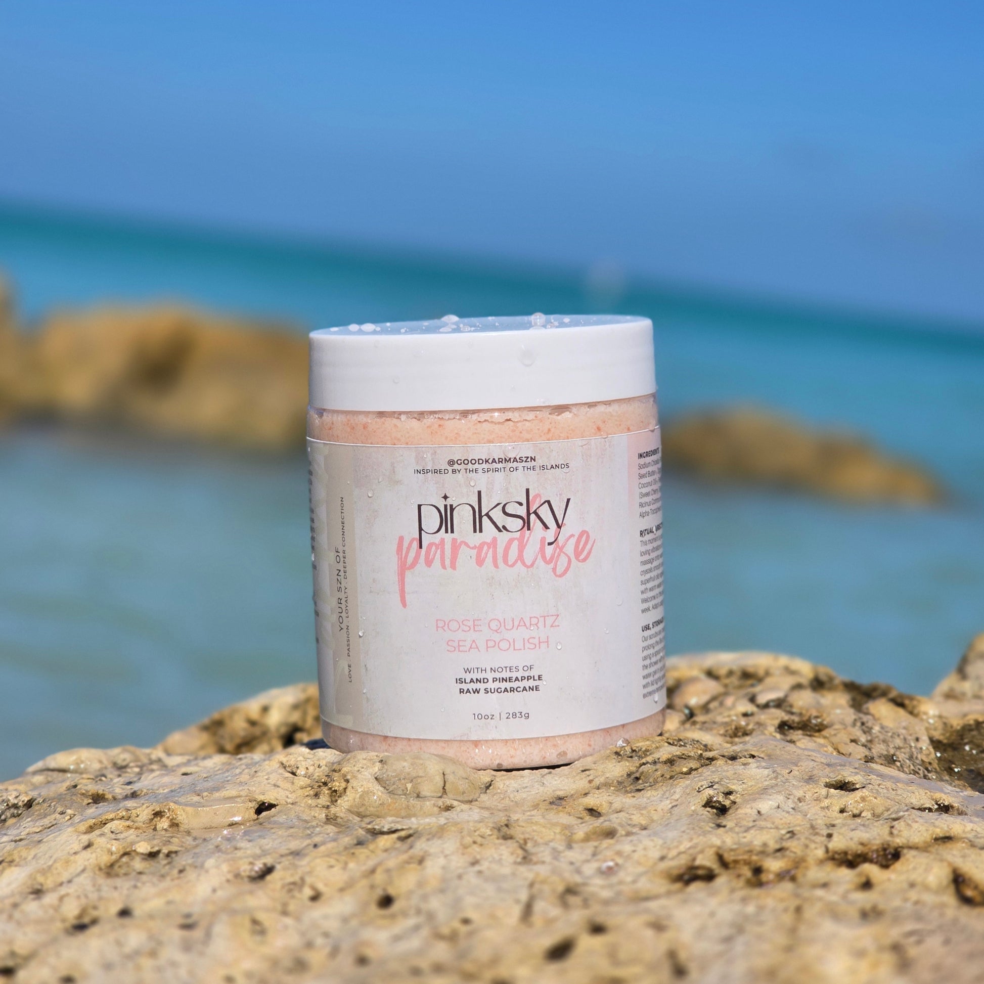 Jar of pinksky paradise pink sea salt scrub on a rock with ocean in the background