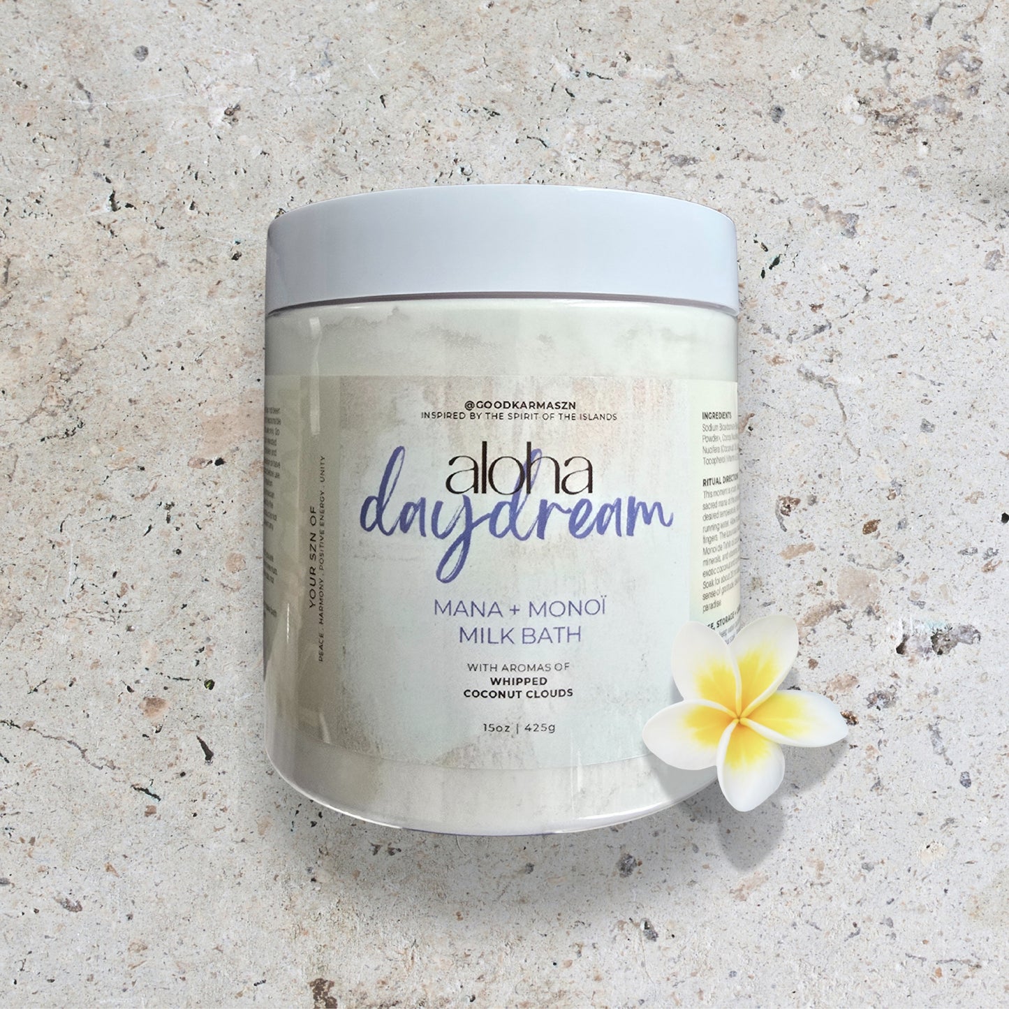 Jar of 'aloha daydream' milk bath on a textured surface with a flower.