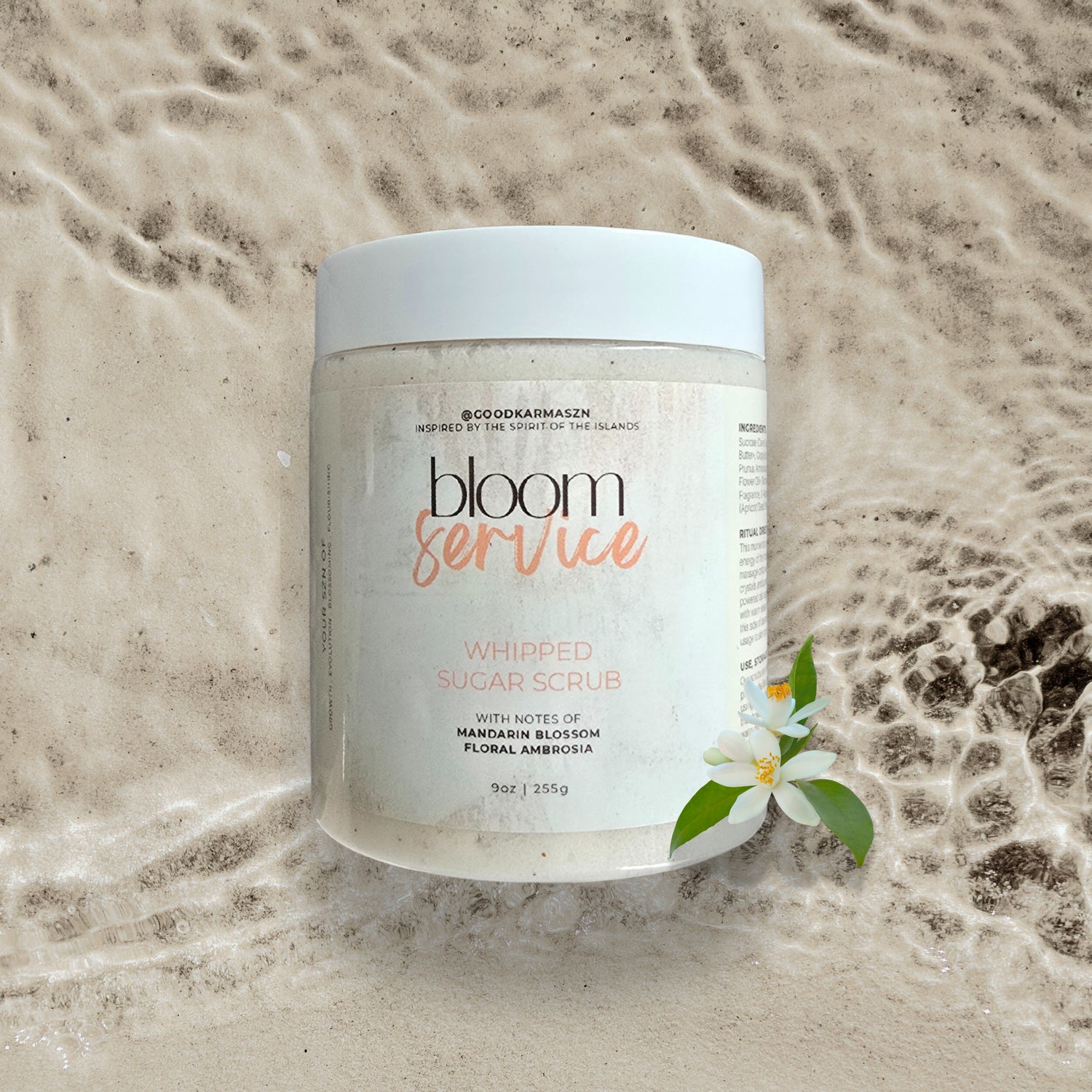 Jar of 'bloom service' whipped sugar scrub with a white orange blossom flower on a textured beige background