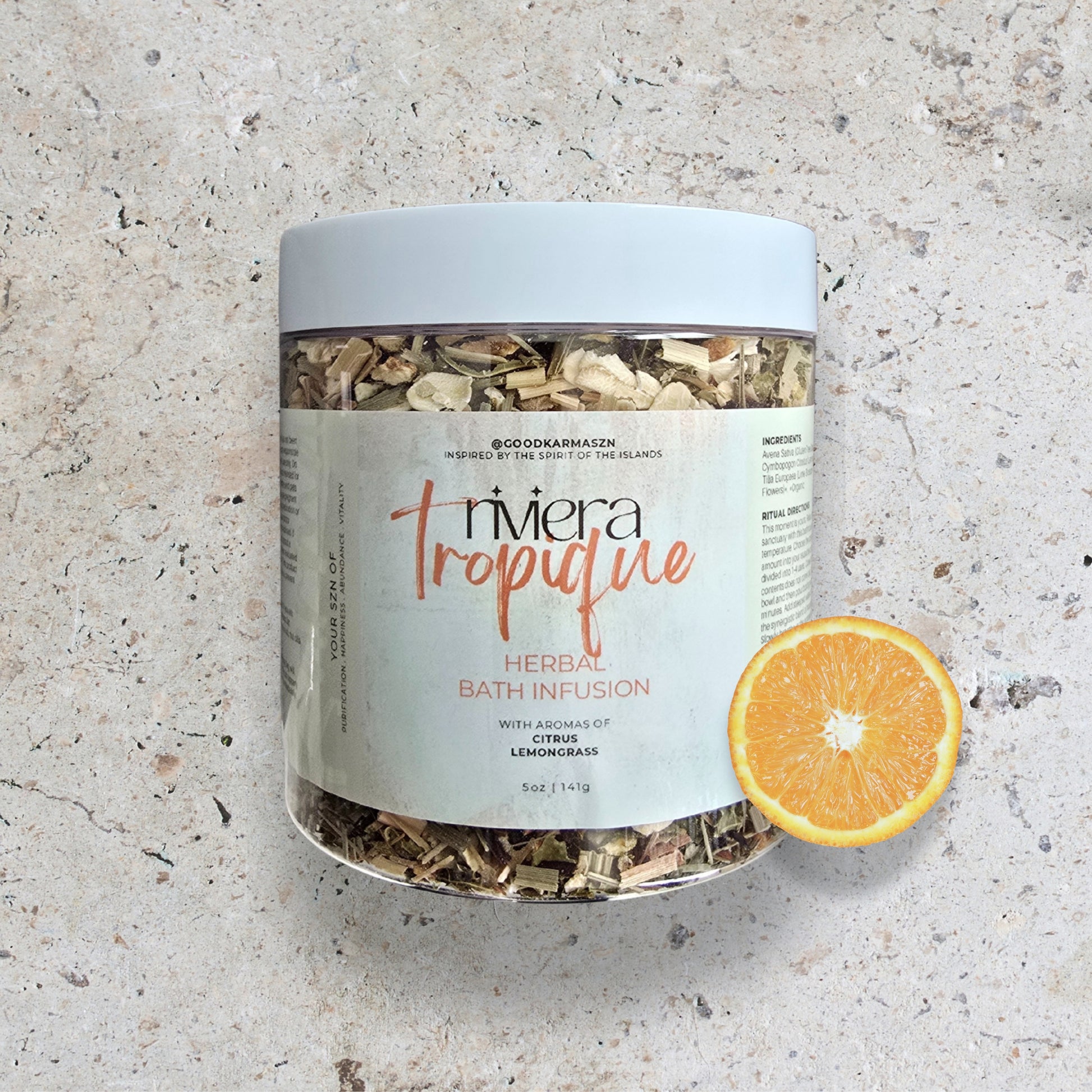 Jar of Riviera Tropique herbal bath infusion with an orange slice on a textured surface