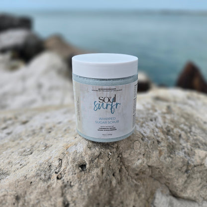 Container of whipped sugar scrub named Soul Surfr on a rock with the ocean behind it.
