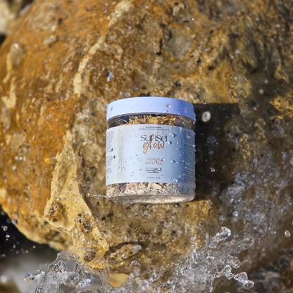 Container of bath tea labeled 'Sunset Glow' on a rock with water splashing around