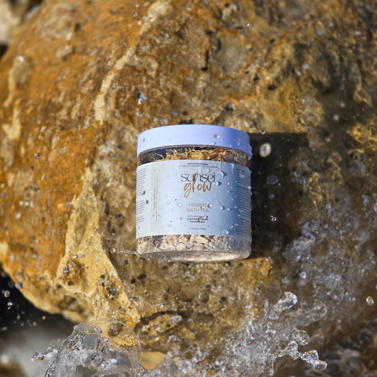 Container of bath tea labeled 'Sunset Glow' on a rock with water splashing around