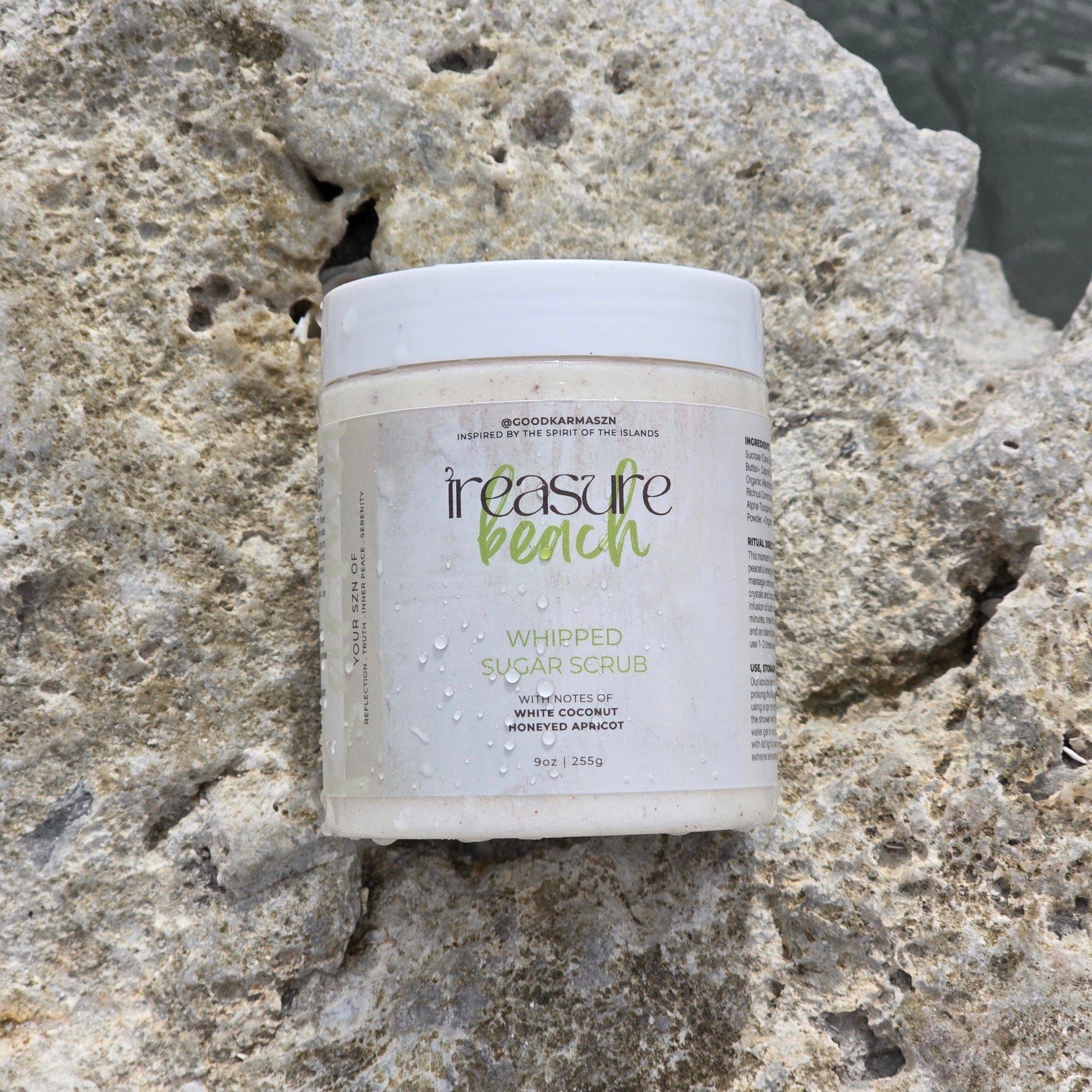 A container of whipped sugar scrub named Treasure Beach on a rocky surface