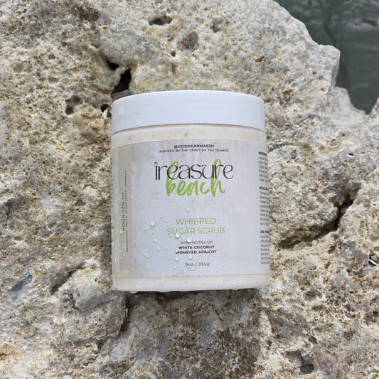 A container of whipped sugar scrub named Treasure Beach on a rocky surface