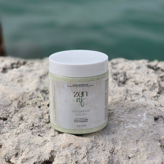 Container of dead sea salt scrub named Zen AF sitting on a rock with ocean water blurred in the backround