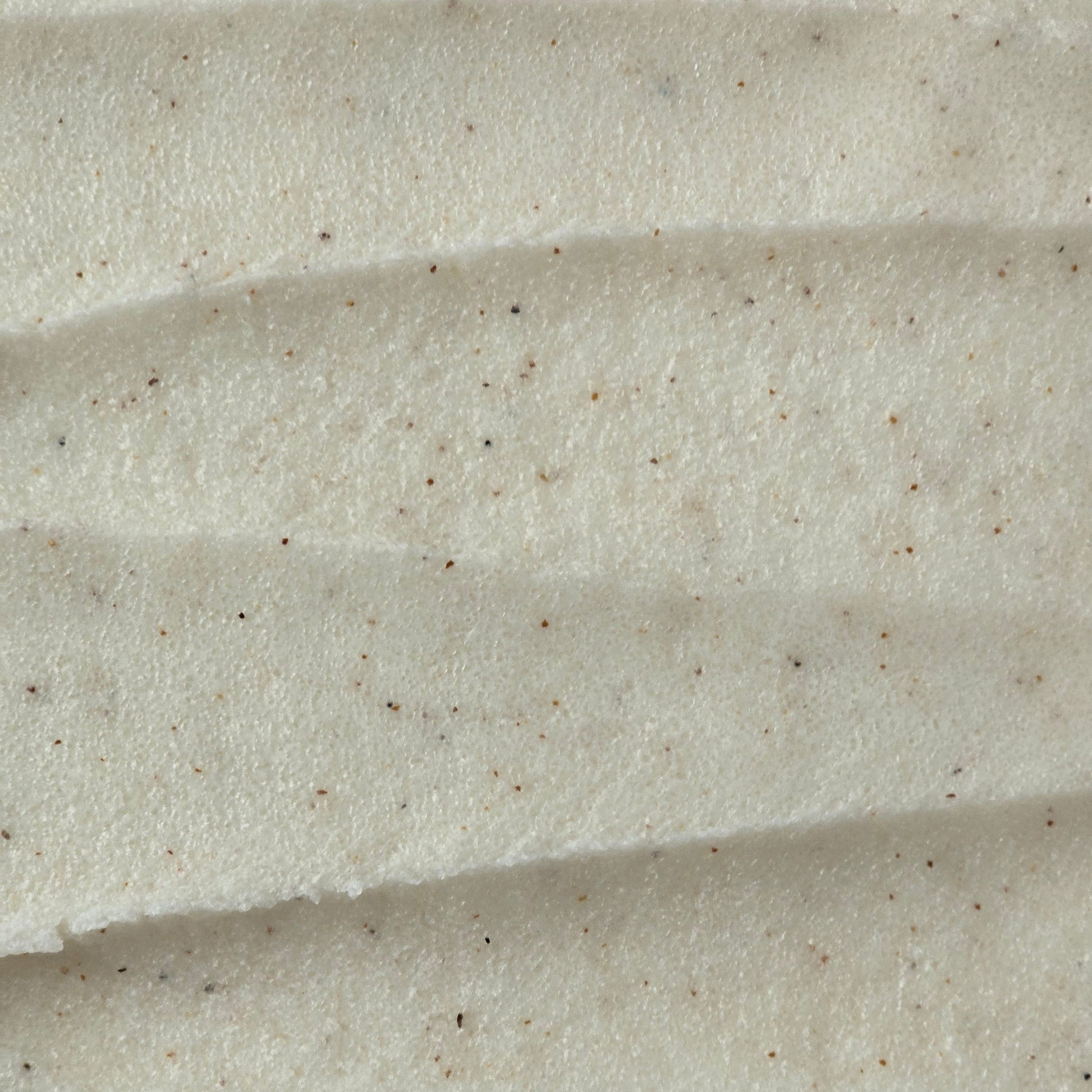 Close up of light cream colored whipped sugar scrub texture with flecks of finely ground apricot seed