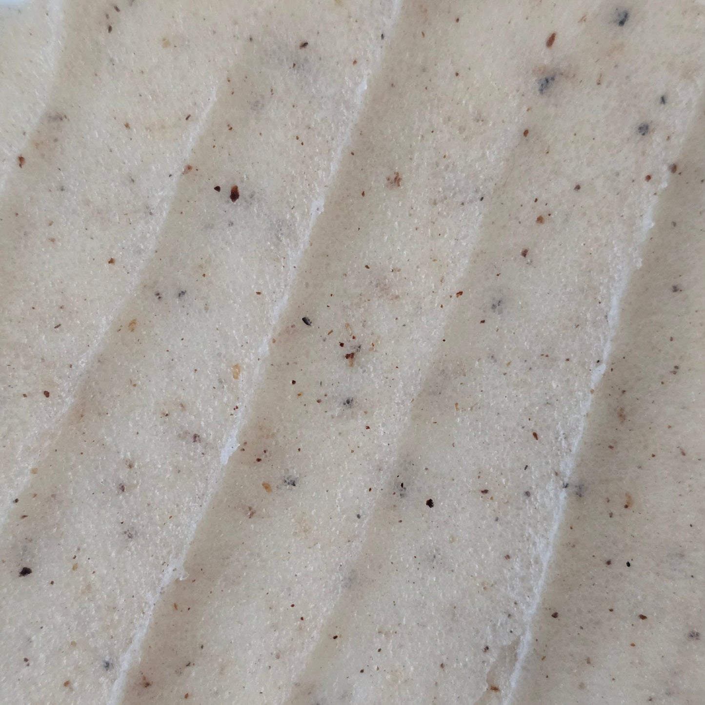 Close up of beige whipped sugar scrub texture with flecks of finely crushed cupuaçu seeds