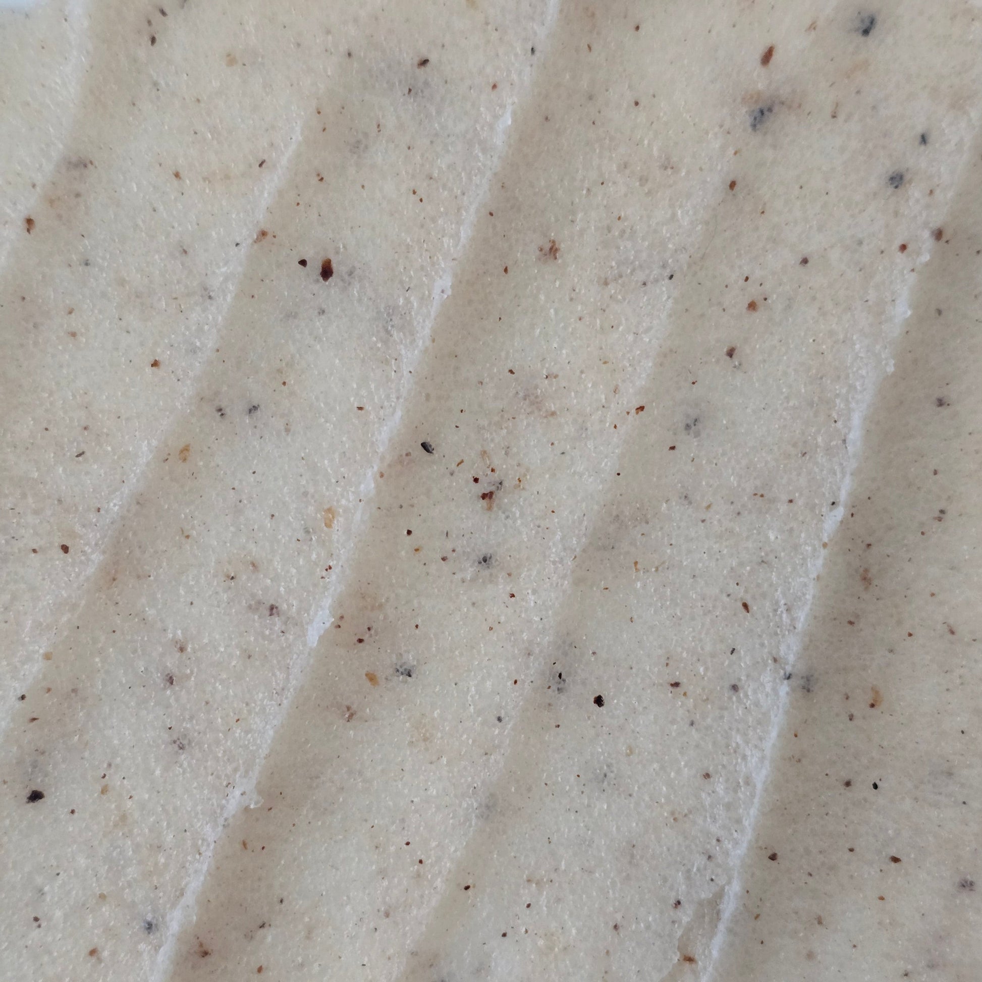 Close up of beige whipped sugar scrub texture with flecks of finely crushed cupuaçu seeds